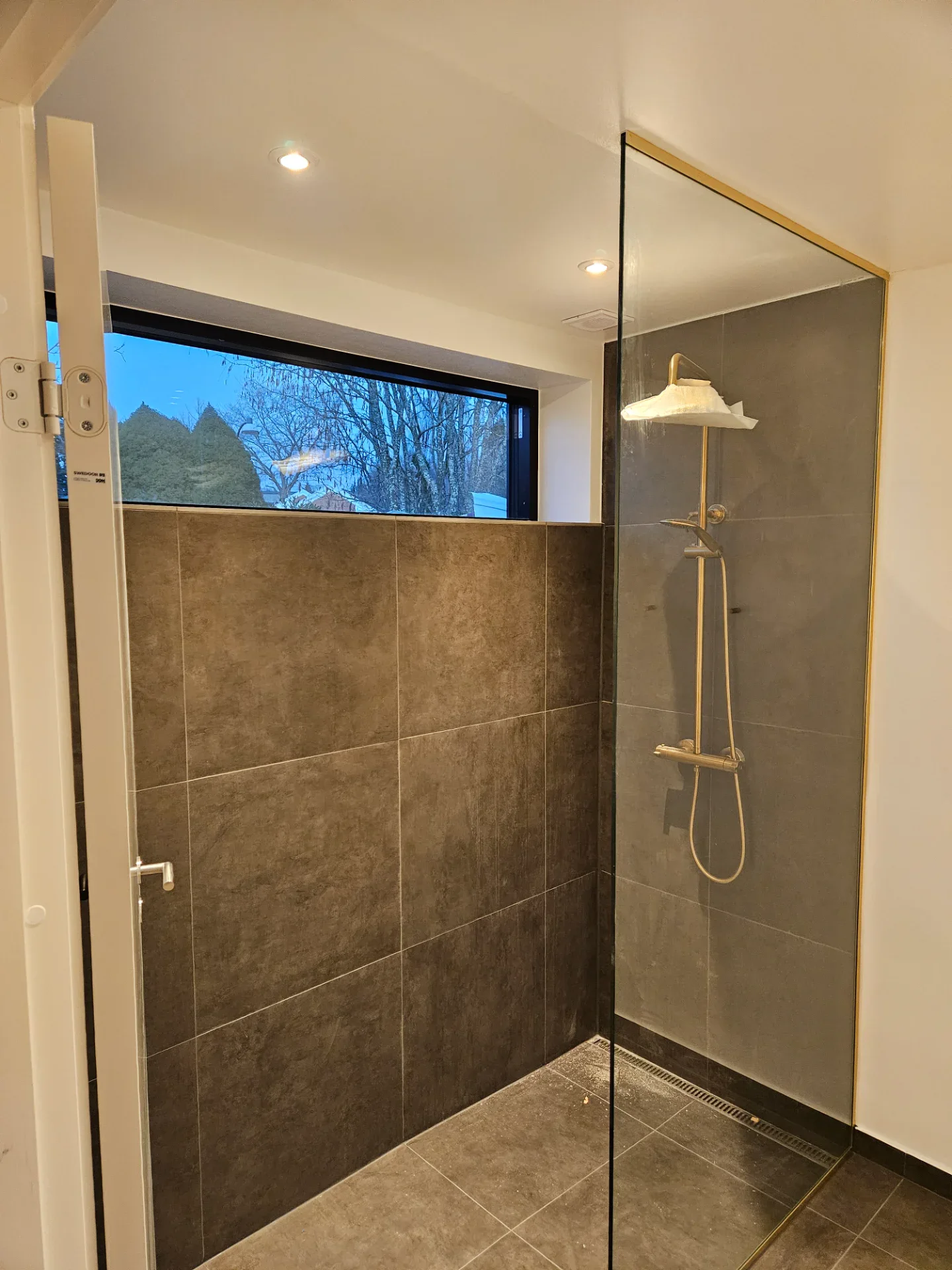 Moderne brusebad med glasdør, vægfliser og håndbruser i badeværelse.